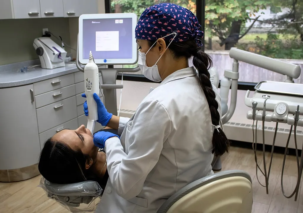 Dentist in surgical cap using an intraoral scanner on a seated patient.