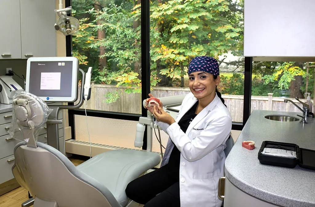 Dentist sitting in a chair in a dental procedure space with a dental chair showing a pair of teeth