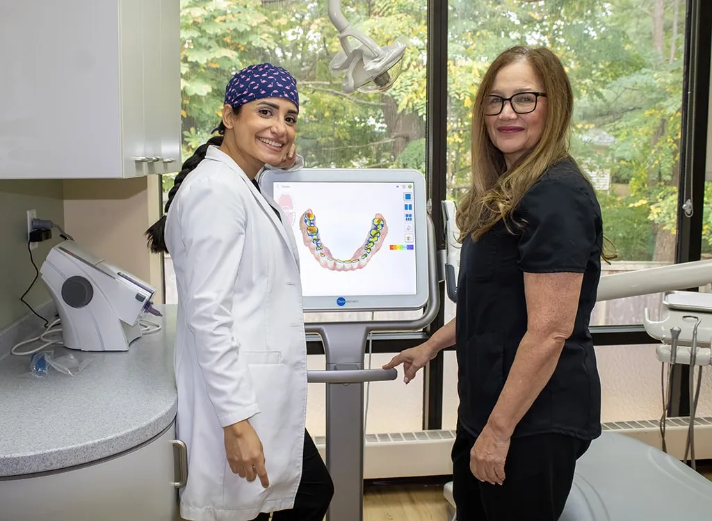 Dentist and staff member standing next to a computer displaying a dental model.