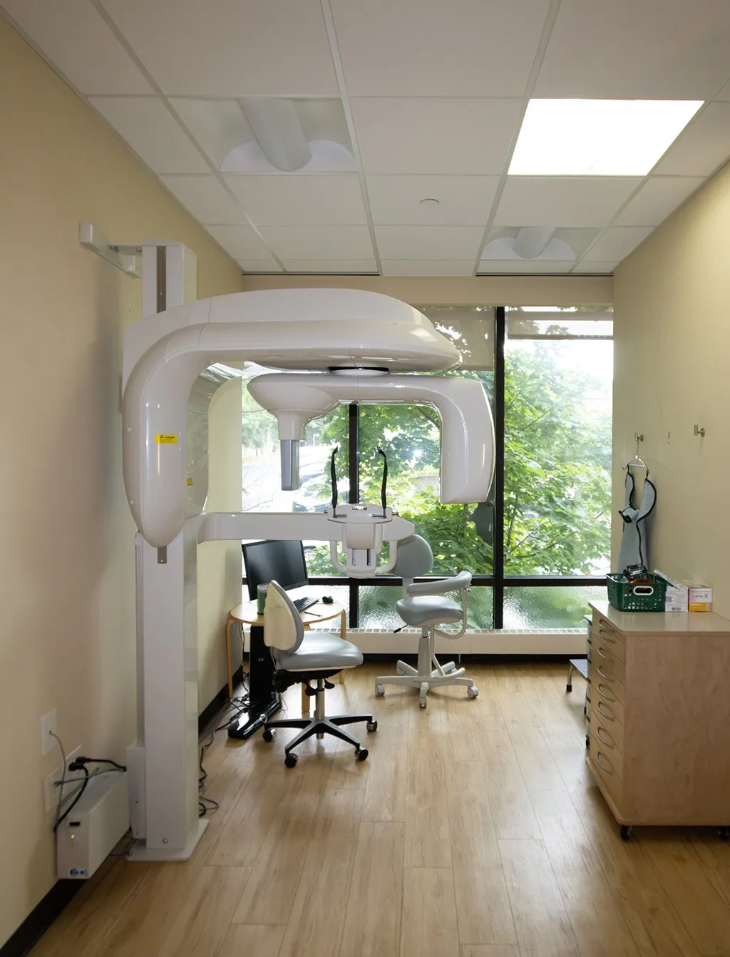 Dental operatory room with panoramic X-ray machine and large window.
