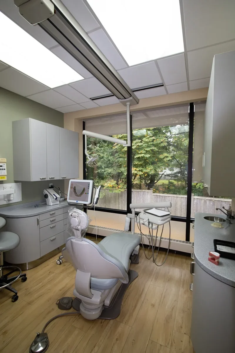 Dental operatory with ceiling-mounted equipment and two monitors.