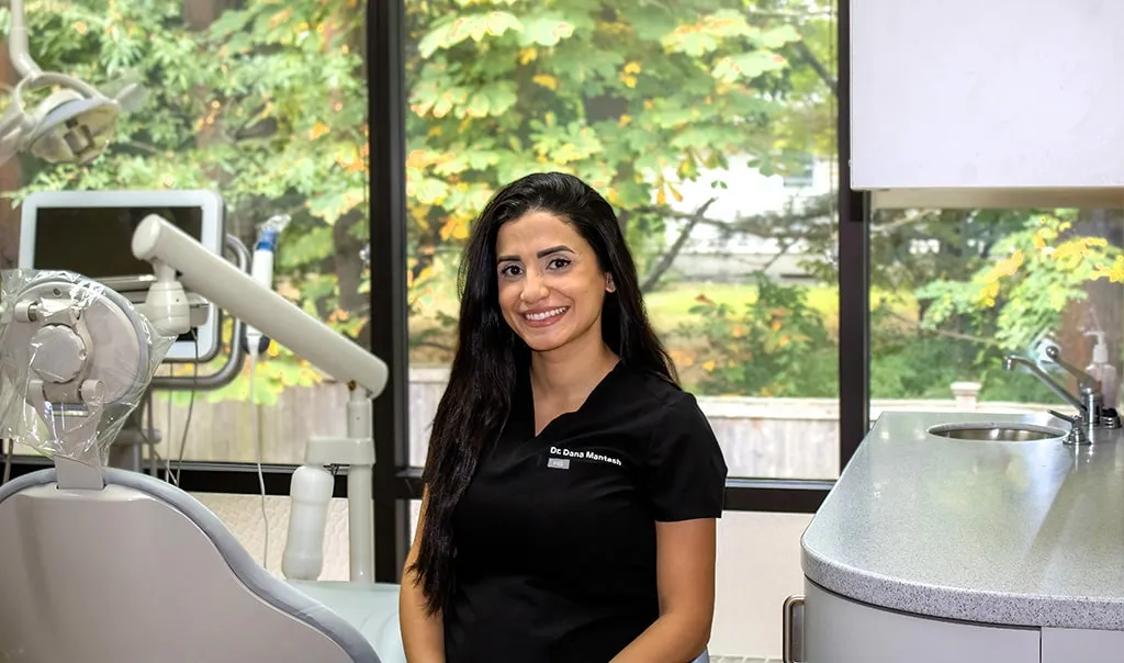 Staff member seated in operatory with dental equipment in background.