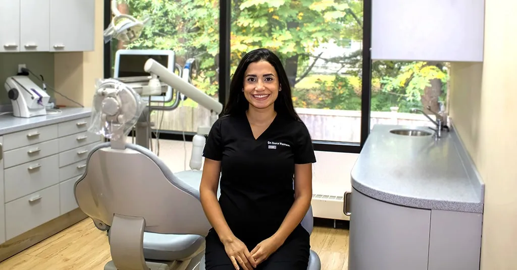 Dentist sitting in a chair in a dental procedure space with a dental chair